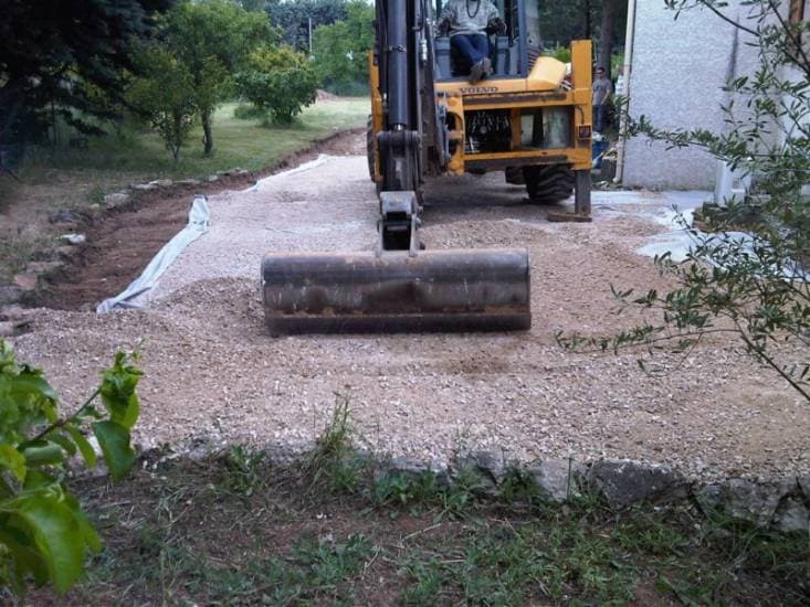 Création d’accès : engin nivelant un lit de grave le long d’une maison